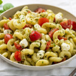 A bowl of caprese pesto pasta salad with basil and utensils. Healthy Food, Real Food, Real Food Recipes, Healthy Food Recipes, Wholesome food, Wholesome food recipes, Whole Food, Whole Food Recipes, Realgood food, Realfooddaily Eat real, Good Real Food, Goodrealfood, pesto, pesto pasta, pasta, caprese pasta, caprese pesto pasta, tomato pasta, pine nuts, cold pasta salad, easy pasta, side dish,