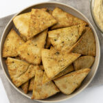 Baked Pita Chips in a bowl, on a tan towel, next to a bowl of hummus. Healthy Food, Real Food, Real Food Recipes, Healthy Food Recipes, Wholesome food, Wholesome food recipes, Whole Food, Whole Food Recipes, Realgood food, Realfooddaily Eat real, Good Real Food, Goodrealfood, pita chips, pita, chips, homemade chips, homemade pita chips, from scratch pita chips, pita chip recipes, easy chip recipes, appetizer, from scratch appetizer
