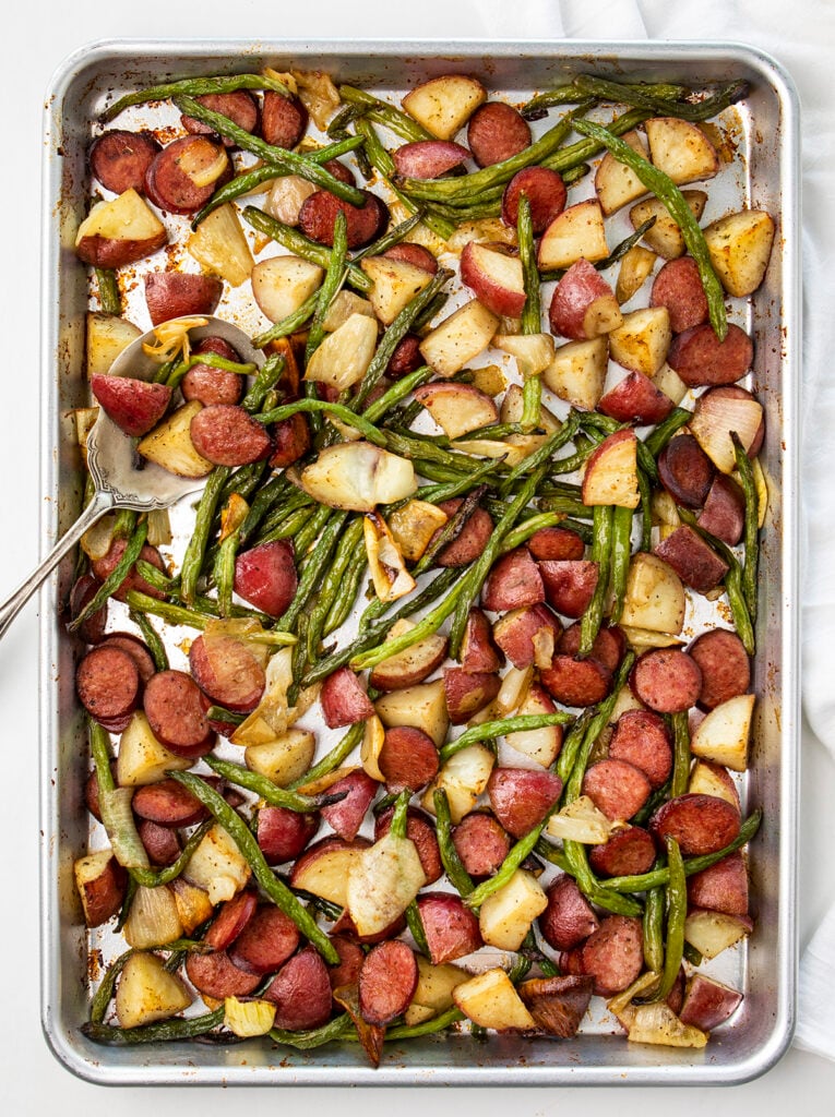 Sheet pan with Cooked sausage, potatoes, green beans, and onions, with a serving spoon. Healthy Food, Real Food, Real Food Recipes, Healthy Food Recipes, Wholesome food, Wholesome food recipes, Whole Food, Whole Food Recipes, Realgood food, Realfooddaily Eat real, Good Real Food, Goodrealfood, sheet pan meals, one pan, sheet pan, one pan meals, roasted veggies, roasted potatoes, roasted green beans, roasted onions, sheet pan sausage, sausage ring recipes, one pan sausage, sheet pan sausage, sheet pan meals, easy meals, under 30, dinner ideas, main course