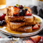 A plate of french toast from the side, topped with berries and being drizzled in maple syrup.