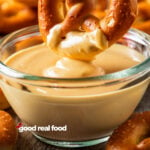 A bowl of cheese sauce with a pretzel being dipped in it.