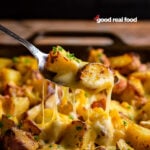 A serving spoon is lifting up a cheesy bite of cheesy roasted potatoes.