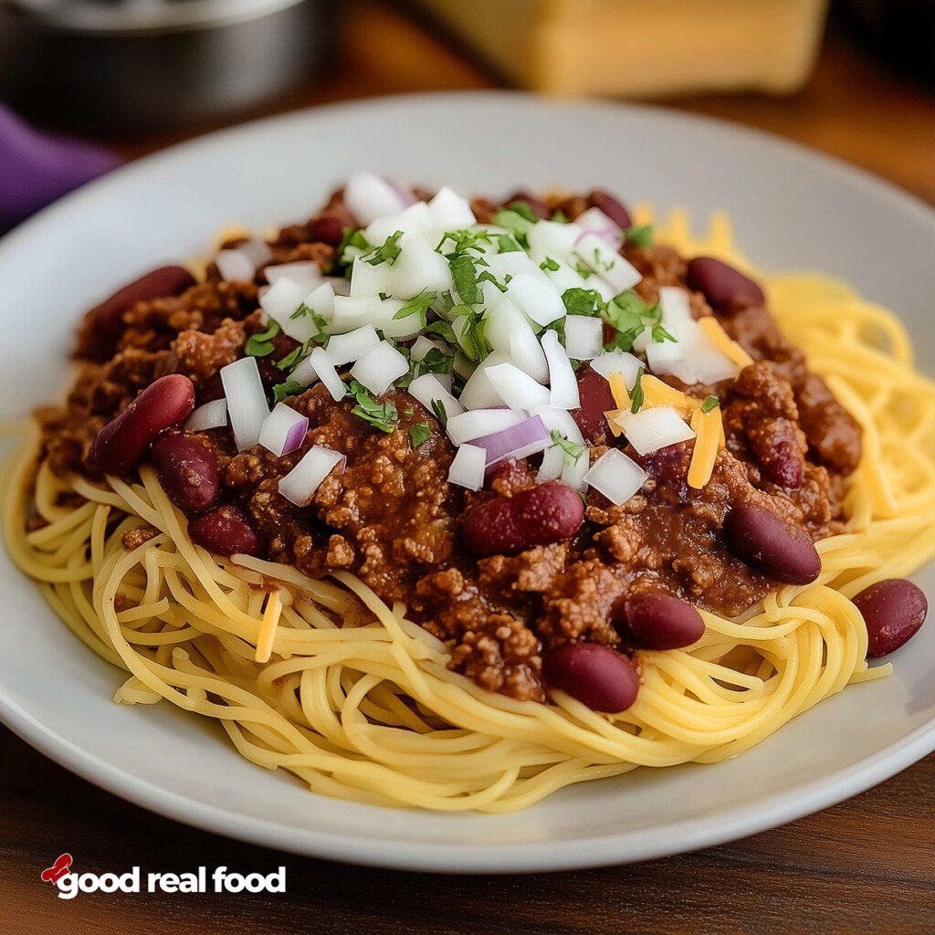 A plate of Cincinnati Chili served over a bed of spaghetti noodles and topped with onions and cheese and beans.