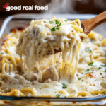 A baking dish filled with turkey tetrazzini, a spoon is lifting a serving out of the dish.