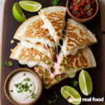 An overhead image of cheese quesadillas with limes, pico, and ranch dipping sauce.