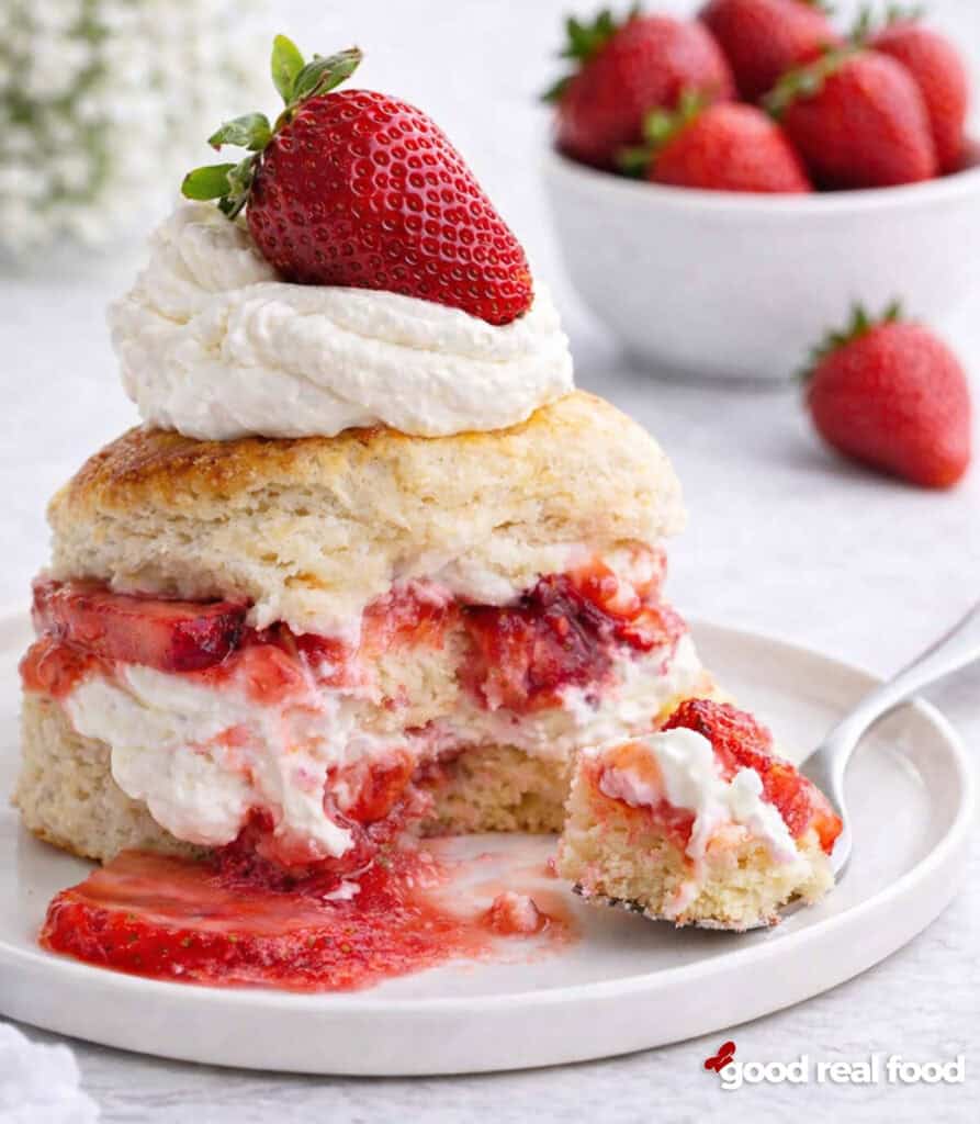 A strawberry shortcake on a white plate with a bite removed.