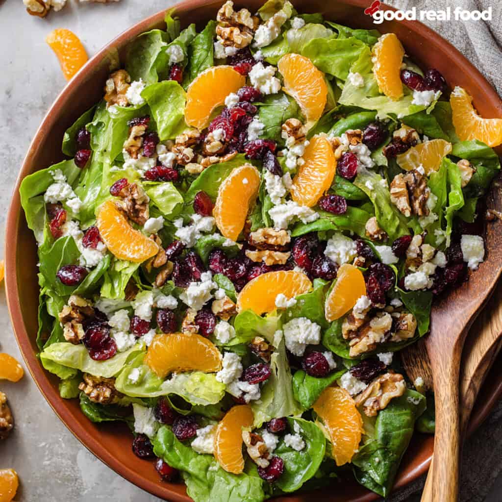 Mandarin salad in a wooden bowl with serving utensils.