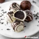 Oreo truffles on a white plate, one truffle is cut open revealing the chocolate interior.
