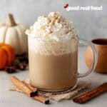 Pumpkin Spice Latte in a glass mug, with fall decor decorating the scene.