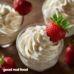 A clear dish filled with cheesecake mousse and garnished with a strawberry.