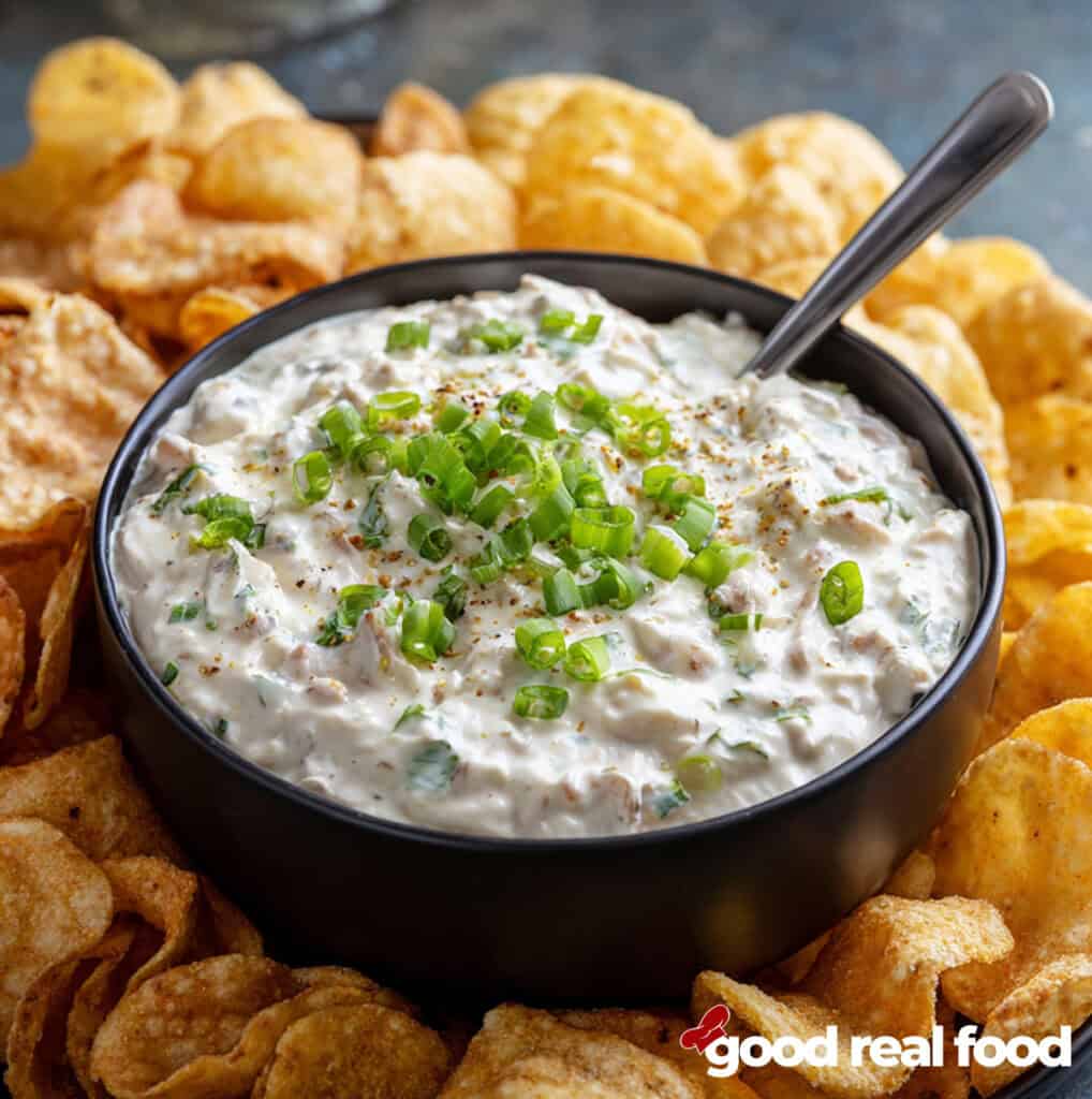 clam dip in a black bowl surrounded by potato chips.