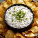 clam dip in a black bowl surrounded by potato chips.