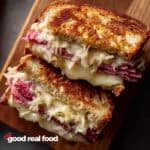 A Reuben sandwich on a wooden cutting board.