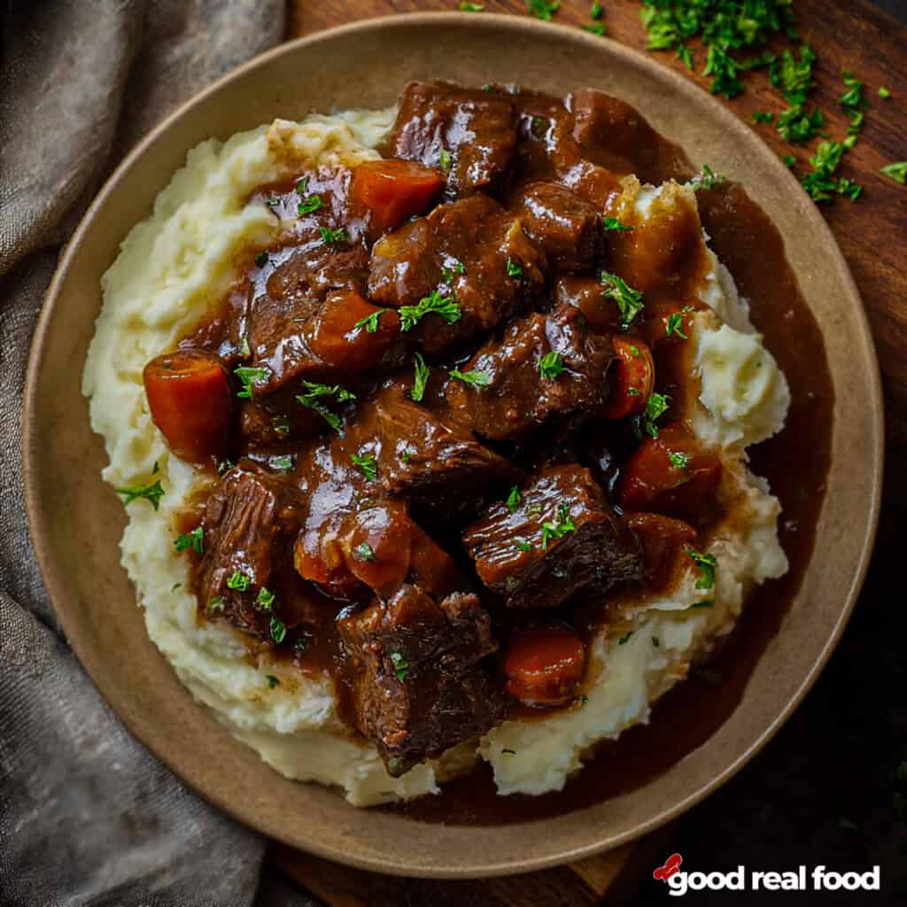 A plate of slow cooker pot roast served over mashed potatoes potatoes.