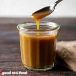A glass jar of homemade butterscotch with a spoon lifting some of the sauce out of the jar.