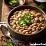 A bowl of pinto beans with jalapeño slices as garnish.