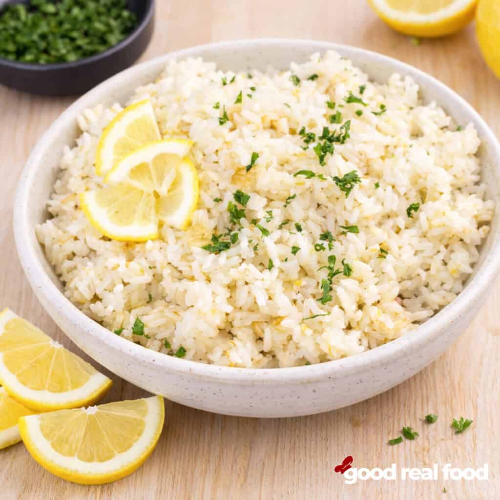 A bowl of lemon rice with fresh lemons and parsley.