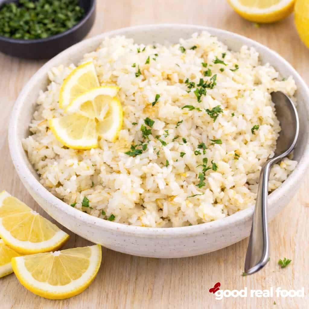 A bowl of lemon rice with fresh lemons and parsley.