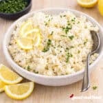 A bowl of lemon rice with fresh lemons and parsley.