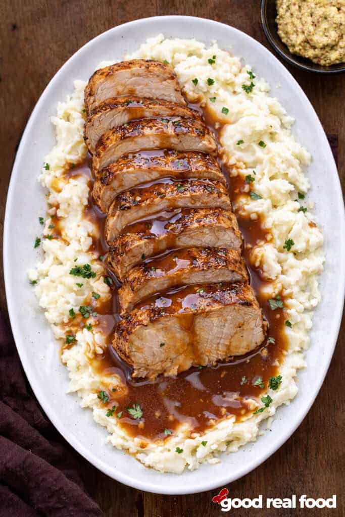 Maple Mustard Pork Tenderloin served over mashed potatoes on a white platter.
