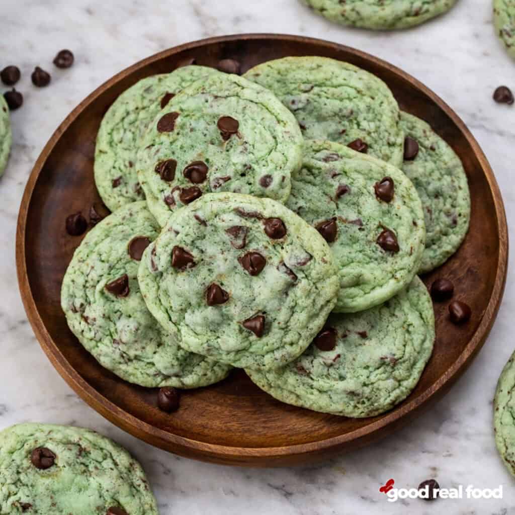 A wooden plate filled with mint chocolate chip cookies.