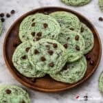 A wooden plate filled with mint chocolate chip cookies.