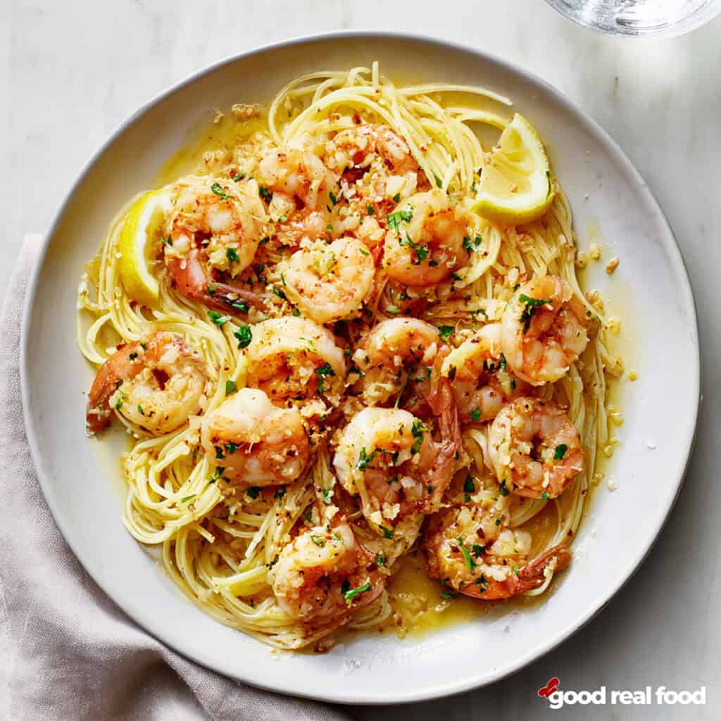 A plate of shrimp scampi served over noodles.