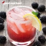 Blackberry Moscato Spritzer in a clear glass garnished with lemons and blackberries.