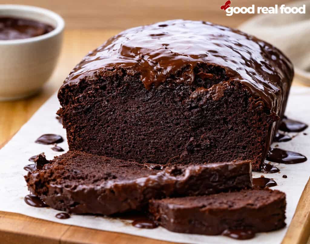 A loaf of brownie bread drizzled with chocolate and partially sliced.