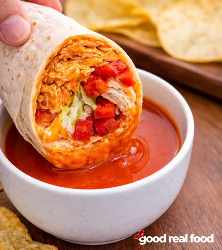 Buffalo Chicken wrap being dunked in buffalo sauce.