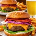 a classic cheeseburger served on a plate with a cold beef in the background.