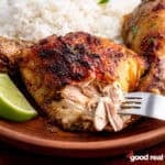 A plate of jerk chicken served with lime and rice.