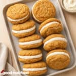 a pan of carrot cake sandwich cookies on a wood counter next to a cloth napkin with a bowl of marshmallow filling