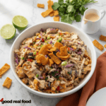 Chicken Cowboy Cabbage In a white Bowl on a white table with fritos, lime, and dressing.