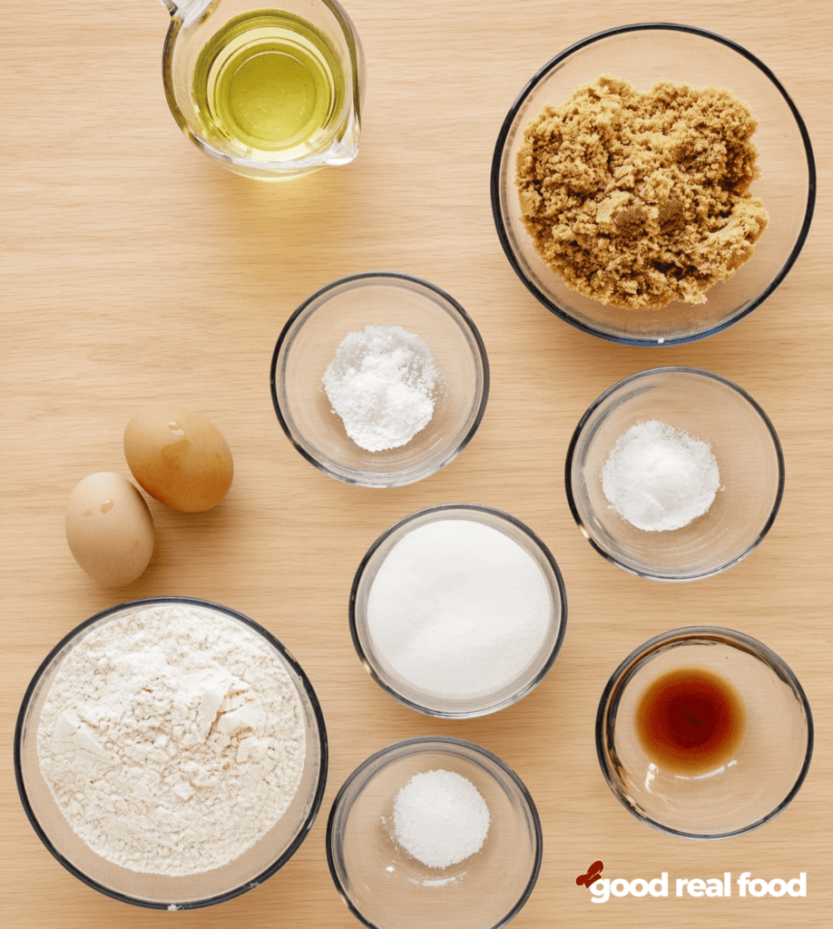 Glass bowls of ingredients Glass bowls of ingredients, flour, salt, brown sugar, baking powder, baking soda, white sugar, vanilla, and two eggs on a wood counter