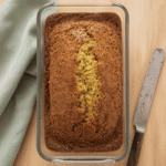 Zucchini Bread in a glass pan on a wood counter next to a knife and a green cloth