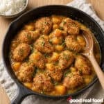 a skillet of crispy coconut peach chicken with a wooden spoon on a cloth napkin on a wood counter