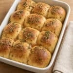a pan of garlic herb cowboy butter rolls next to a cloth napkin on a wood counter