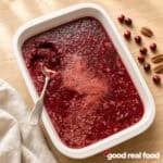 Holiday Cranberry Jello Salad in a white dish with a silver serving spoon on a wood counter next to a cloth napkin and some cranberries and pecans