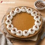 holiday pumpkin cheesecake on a piece of parchment and a wire rack next to a cloth napkin, knife, and a bowl of pecans