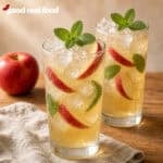 two sparkling Apple cider Mojitos' with mint and apple garnish on a wood counter next to a cloth napkin and an apple