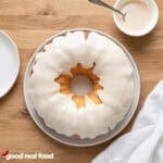 Vanilla Bundt Cake with Vanilla Glaze pictured from above next to a white plate, a cloth napkin, and a small bowl of glaze