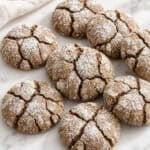 many scattered chewy gingerbread crinkle cookies next to a cloth on a marble counter