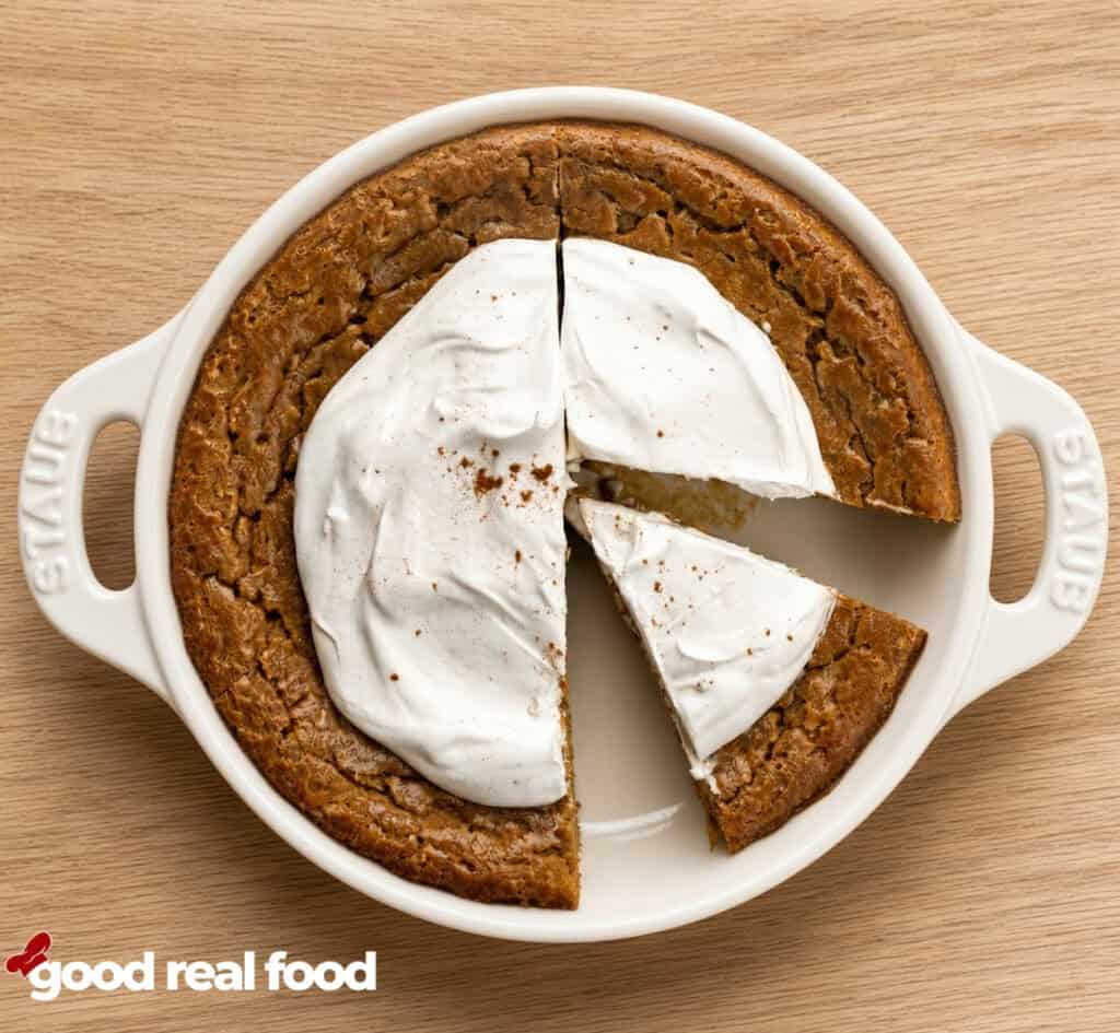 a pan of crustless pumpkin pie with whipped cream with a slice taken out and a slice separated from the rest of the pie on a wood counter