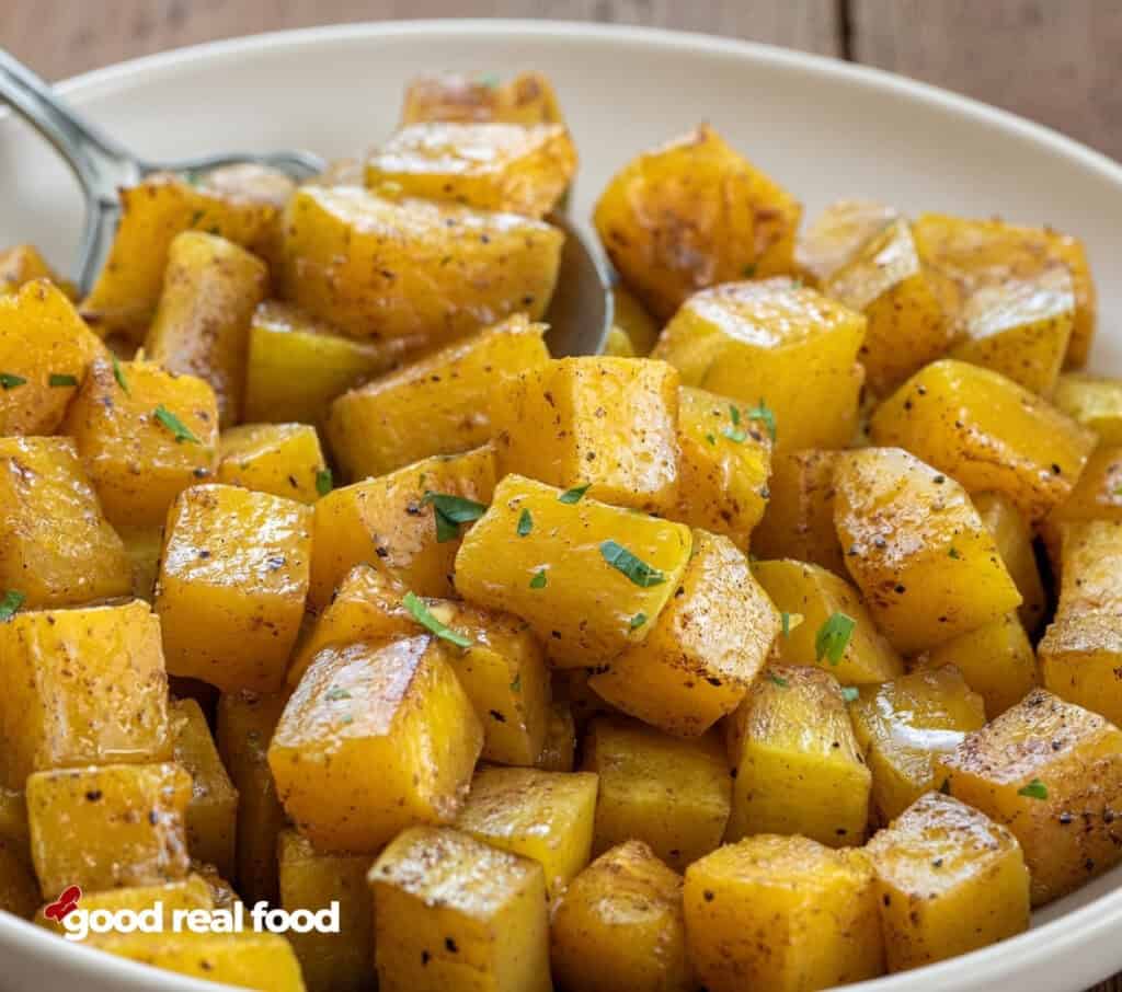 a close up of Maple Cinnamon Roasted Squash in a white bowl a close up of Maple Cinnamon Roasted Squash in a white bowl with a silver spoon