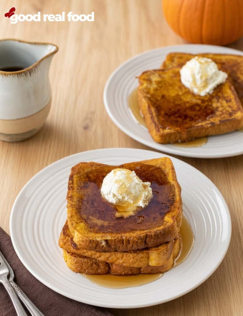 two plates with stacks of pumpkin pie spice French toast on a wood counter two plates with stacks of pumpkin pie spice French toast on a wood counter next to a cloth napkin with two forks and a pumpkin in the background